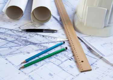 Blueprints, pens, pencils, rulers, and paper laid out on a table