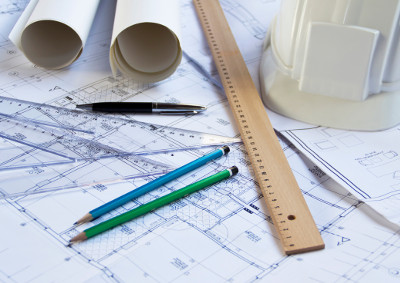 Blueprints, pens, pencils, rulers, and paper laid out on a table